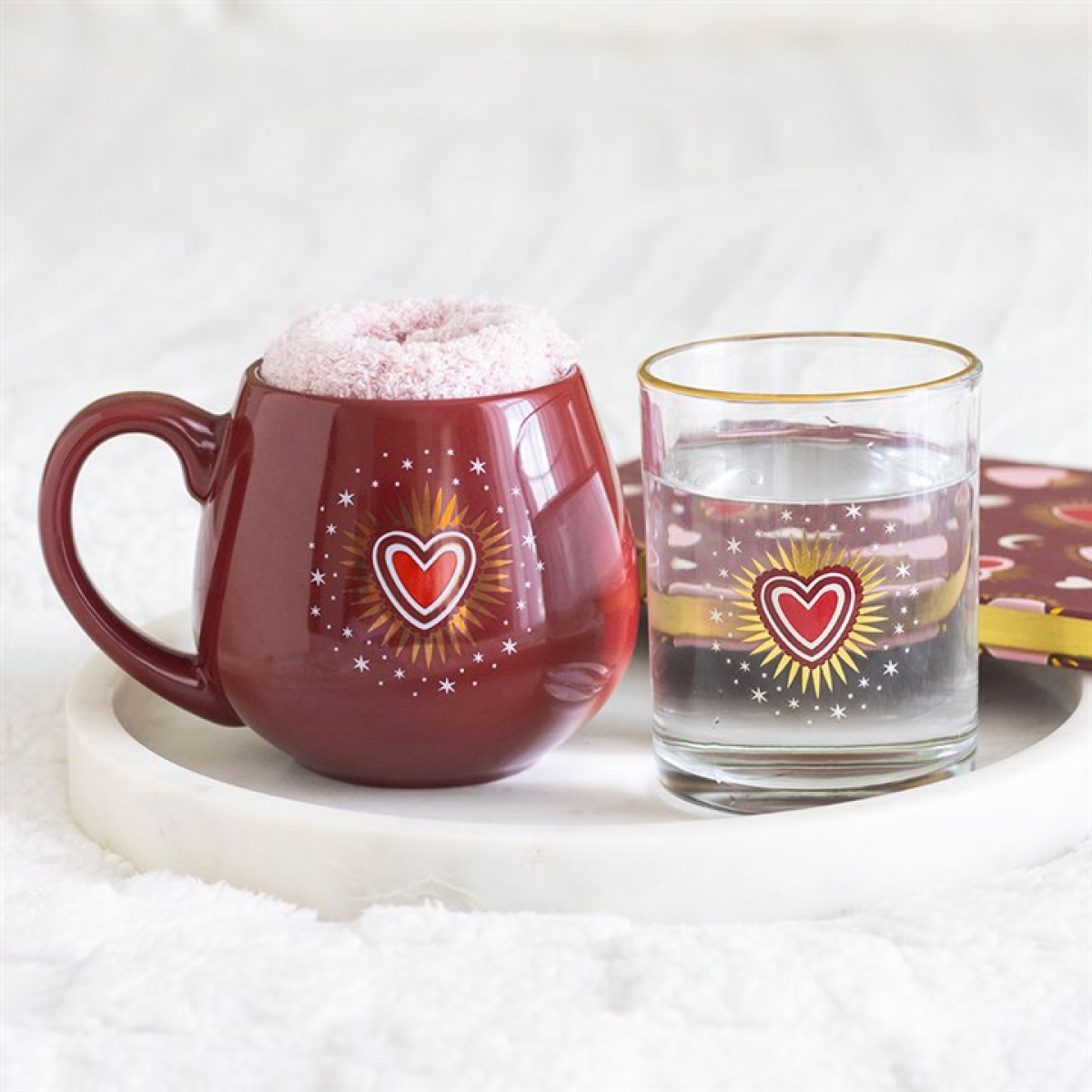 Clear water glass with a red sacred heart design and gold rim accent. Presented alongside a red rounded mug and socks set from the same range.