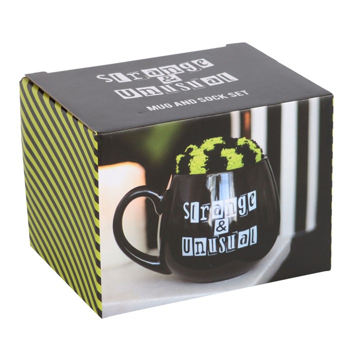 Black rounded ceramic mug with 'Strange & Unusual' text and a pair of complementing green and black striped cosy socks. Presented in themed box.