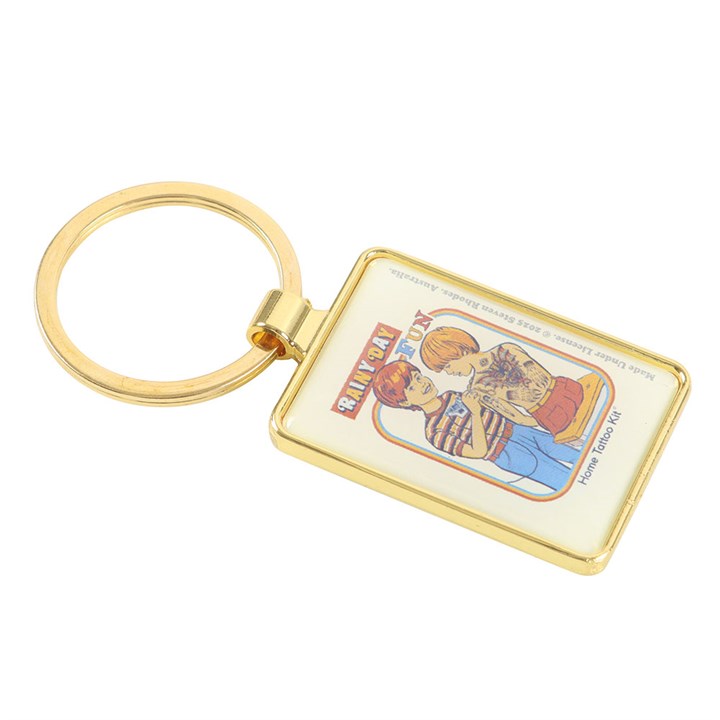 Steven Rhodes enamel keyring depicting a young boy tattooing his younger brother with a home made tattoo kit. Text reads Rainy Day Fun.