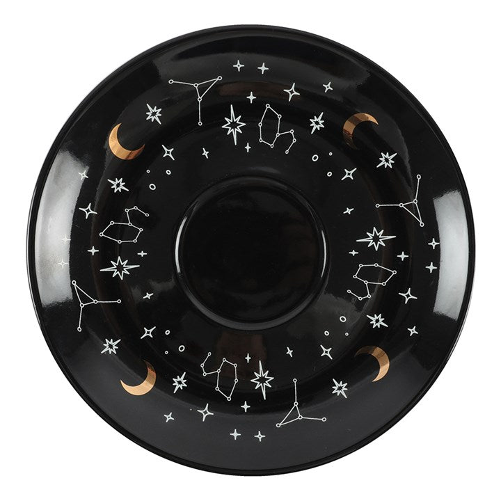 A white teacup with contrasting black saucer, finished with tea-reading illustrations. Sold with a guide for interpretation. Close up on saucer design.