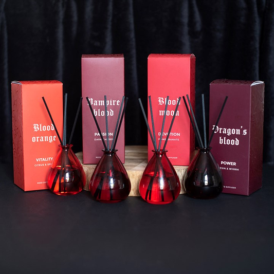 Four gothic inspired reed diffusers. One each of an orange bottle, purple bottle, pink bottle and black bottle. 