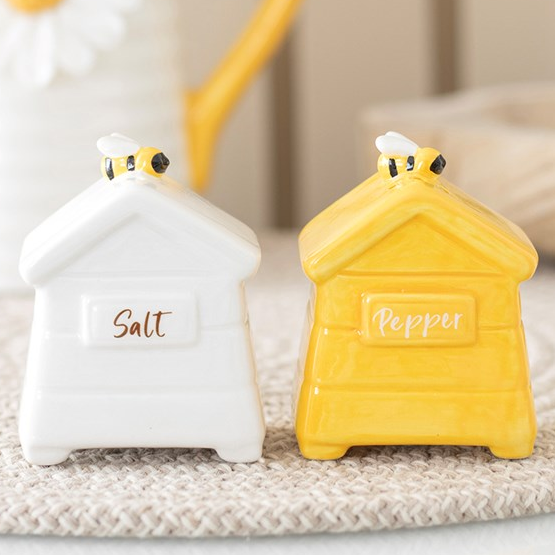 A set of white and yellow ceramic salt and pepper shakers, shaped like traditional beehives with a bee sitting on top. 