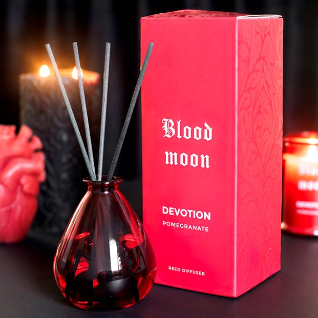 Blood Moon reed diffuser, including deep pink teardrop-shaped glass bottle and reeds. 