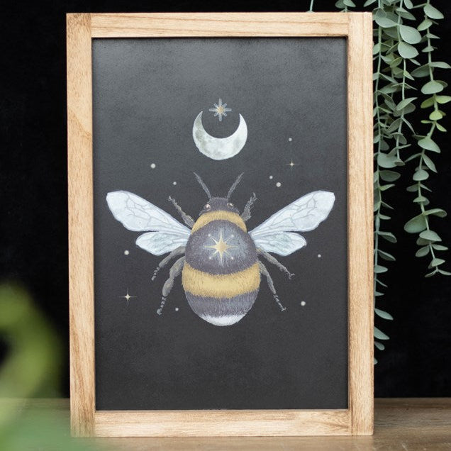Framed wall art depicting a plump forest bee with crescent moon and celestial 
accents on a black background.