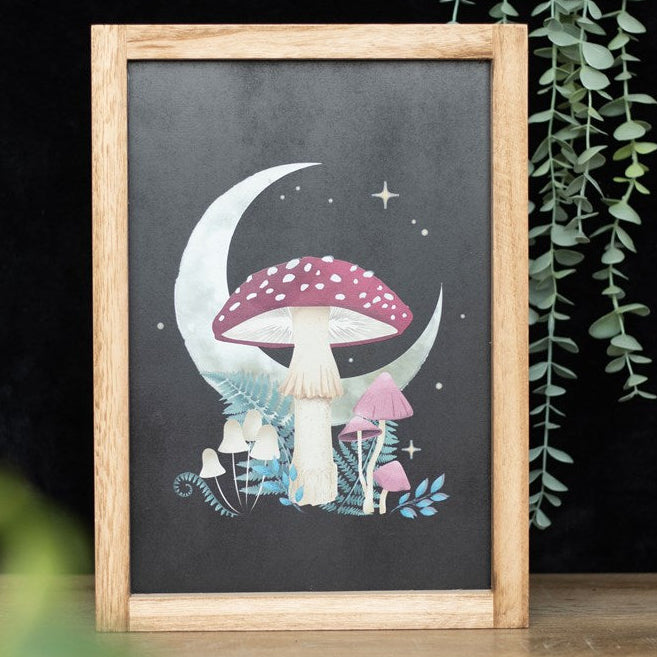 Framed wall art depicting a magical forest mushroom, a crescent moon, vintage style fauna and celestial accents on a black background. 