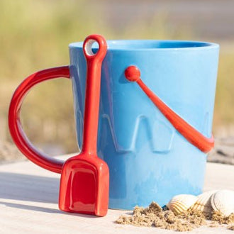 Blue ceramic sandcastle bucket-shaped mug with red spade-shaped teaspoon.