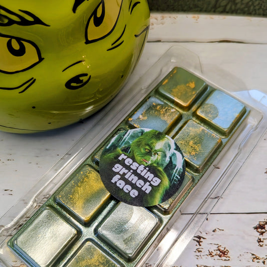 Resting Grinch Face coconut wax melt. Deep green snap bar with golden shimmer accents.