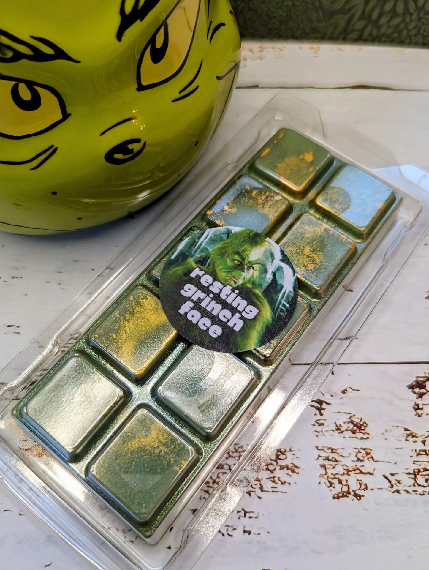 Resting Grinch Face coconut wax melt. Deep green snap bar with golden shimmer accents.