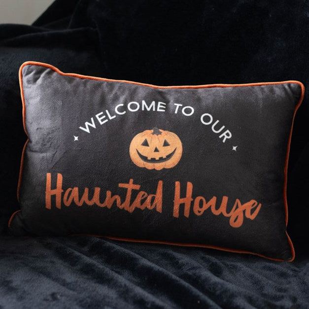 Rectangular Halloween throw cushion. Black background with an orange trim, Welcome to our Haunted House text and jack o' lantern motif.