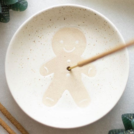 Ceramic incense dish featuring a smiling gingerbread man on a speckled, off white background. 