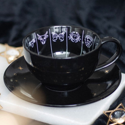 Black ceramic teacup and saucer set, designed with astrology wheel illustrations and sold with a tea leaf reading guide.