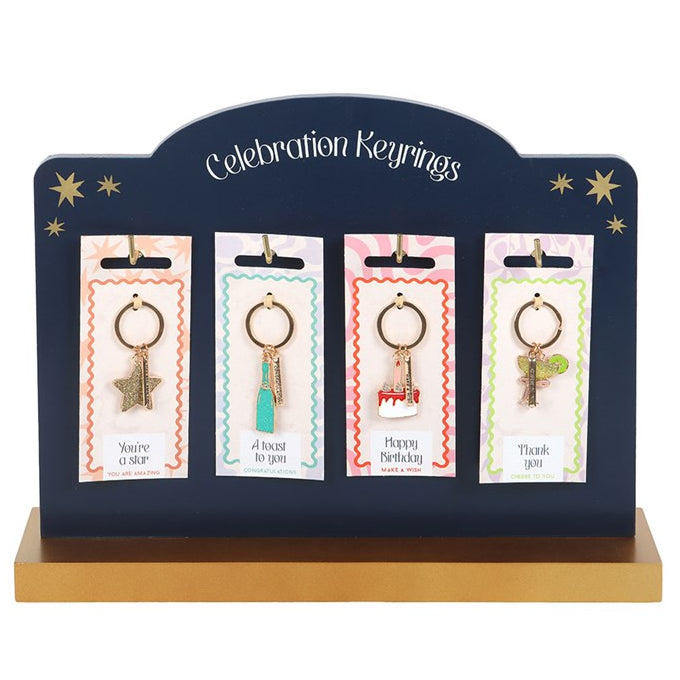 Set of 24 enamel party-icon keyrings. Champagne bottle, cocktail glass, star and birthday cake. Presented on a blue stand.