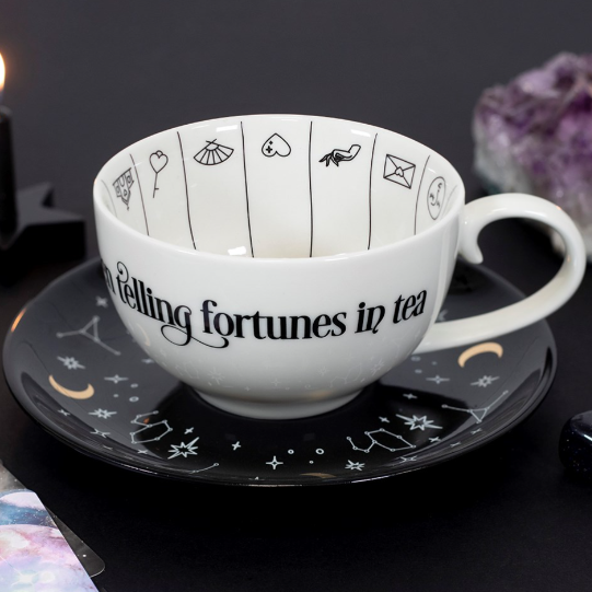 A white teacup with contrasting black saucer, finished with tea-reading illustrations. Sold with a guide for interpretation. 